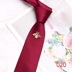 Detail view of a burgundy men's necktie featuring an elegant gold pearl bee brooch decoration.