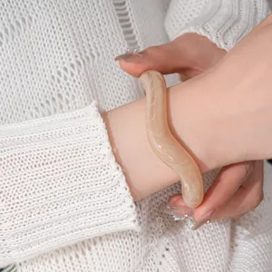 Close-up detail of a minimalist beige irregular wavy acrylic open bracelet worn on wrist.