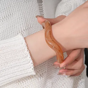 Detail view of the brown marbled acrylic wavy bangle worn on wrist, showcasing unique texture and polish.