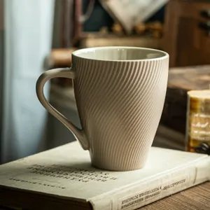 Mug en céramique beige minimaliste avec rayures gaufrées posé sur un livre vintage