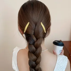 Vista detallada de una horquilla dorada minimalista para el cabello con trenza elegante.