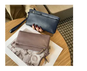 Leather clutch bag detail view featuring dual zipper pockets and handy wrist strap design.