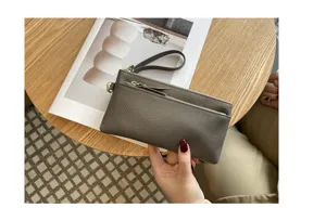 Detailed view of grey leather clutch bag showing textured finish and functional double zippers.