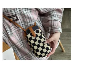 Kleine crossbody telefoontas van canvas met zwart-wit schaakbordpatroon en lederen riem.