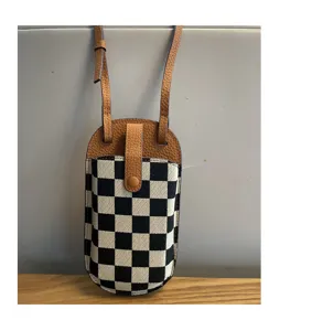 Detailopname van zwart-witte ruitjes canvas telefoontas met bruine lederen schouderriem.