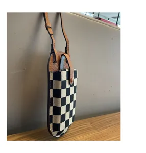 Detailopname van zwart-wit geruit canvas telefoontasje met bruine lederen schouderband.