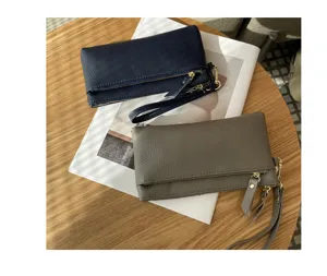 Detailed view of genuine leather wristlet clutch wallets in navy and taupe with metal zippers.