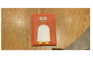 Nahaufnahme des niedlichen orangefarbenen Lederkartenetuis mit witzigem Pinguin-Design.