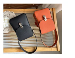 Detail view of mini leather phone bags in black and orange, featuring metal lock and handle.