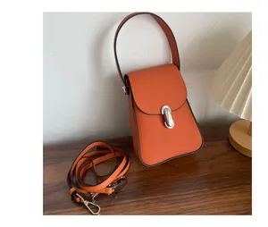 Detailed view of orange leather phone bag, minimalist vertical crossbody design with metal clasp.