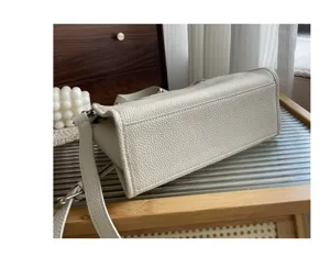 Vue détaillée du sac à bandoulière en cuir crème avec texture grainée fine et détails métalliques.