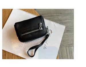 Close-up detail of black leather mini coin purse with double zippers and wrist strap.