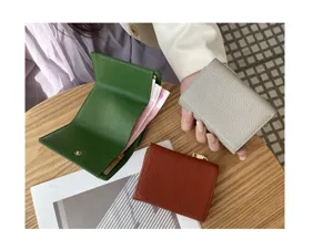 Detailed view of women short tri-fold genuine leather wallets in multiple colors on wooden table.