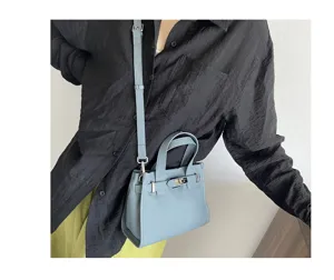 Sac à main bandoulière en cuir véritable bleu clair avec fermoir tournant et poignée.