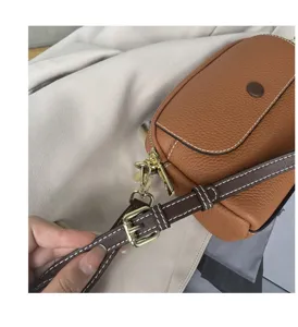 Close-up detail of women's brown leather crossbody bag strap, golden hardware and neat stitching.