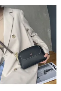 Detail shot of a black genuine leather crossbody bag held by a model in beige blazer.