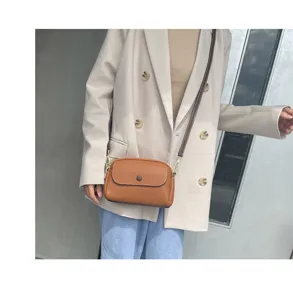 Detail shot of a brown leather crossbody bag worn by a model in a beige blazer style.