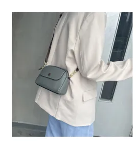 Detailed view of a chic gray leather crossbody shoulder bag with brown strap worn by a model.