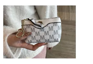 Close-up detail of white mini coin purse with M monogram pattern and gold zipper ring.