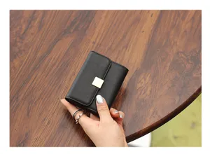 Vista detallada del mini tarjetero negro con cierre metálico dorado sobre madera.