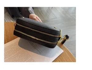 Black leather camera bag detail view, double zip compartments and golden metal hardware.