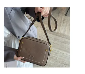 Detail shot of brown leather crossbody bag with metal H clasp and white contrast stitching.