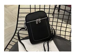 Close-up detail of black leather mini crossbody phone bag with zipper and silver hardware.