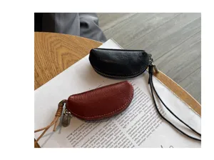 Detailed shot of mini half-moon leather coin pouch with zipper and wrist strap on paper.