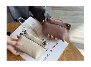 Close-up detail of mini genuine leather coin purse with zipper and wrist strap in soft colors.