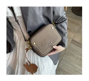 Brown leather crossbody camera bag with metal H clasp, white stitching and cute rabbit charm.