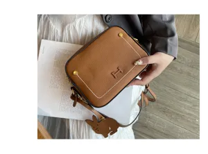 Brown genuine leather shoulder camera bag with chic rabbit charm and stylish metal accent.