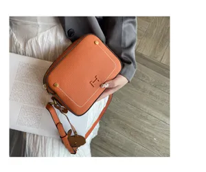 Stylish orange leather camera bag with H hardware, white stitching, and adjustable shoulder strap.