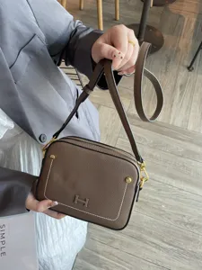 Stylish brown leather camera bag with metal H logo, chic crossbody shoulder bag for women.