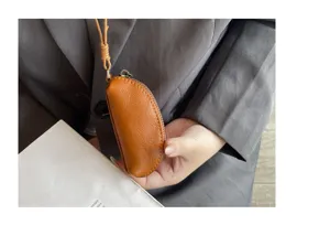 Detail view of mini brown leather coin purse hanging by a cord, held securely in hand.