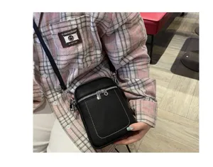 Close-up of black mini leather phone bag, detailed zipper pocket and contrast stitching.