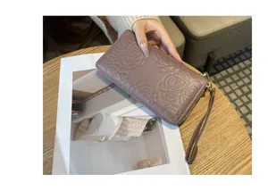 Genuine leather long wallet detail showing embossed camellia flower pattern and wrist strap.