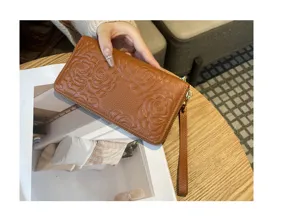 Detail view of embossed camellia leather long wallet in brown with zipper and wrist strap.