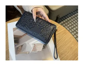 Close-up detail of a dark blue leather long wallet with embossed camellia design and strap.