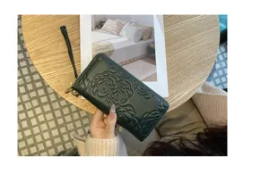 Detail view of dark green embossed camellia leather long wallet with wrist strap.