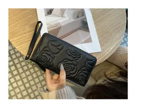Detail view of black leather long wallet with embossed camellia flower and wrist strap.