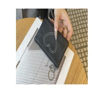 Black leather coin purse detail close up showing heart stitch design and metal zipper pull.