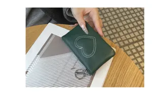 Close-up detail of dark green leather coin purse with cute heart stitching and metal ring.