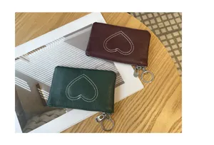 Detailed shot of two compact leather coin purses with stitched heart design on a wooden table.