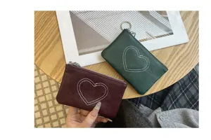 Detail shot of genuine leather coin purses featuring stitched heart patterns in wine red and green.