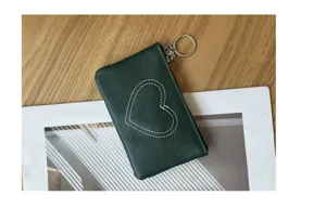 Close-up detail of the dark green leather coin purse featuring white stitched heart motif.