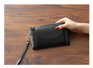 Detailed view of the black leather clutch bag, featuring a wrist strap and envelope pocket.