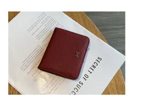 Detail shot of a compact burgundy leather wallet with metallic H logo on wooden background.