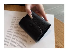 Détail de porte-cartes accordéon en cuir noir, design compact à bouton-pression, style minimaliste.