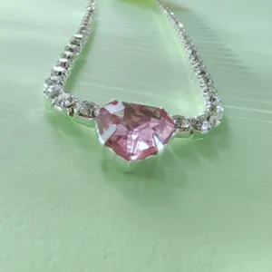 Collier choker de couleur argentée avec un cristal de cœur rose et une chaîne de strass.