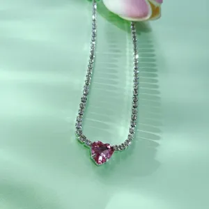 Vue détaillée d'un collier ras de cou tennis en cristal cœur rose vif sur fond vert.